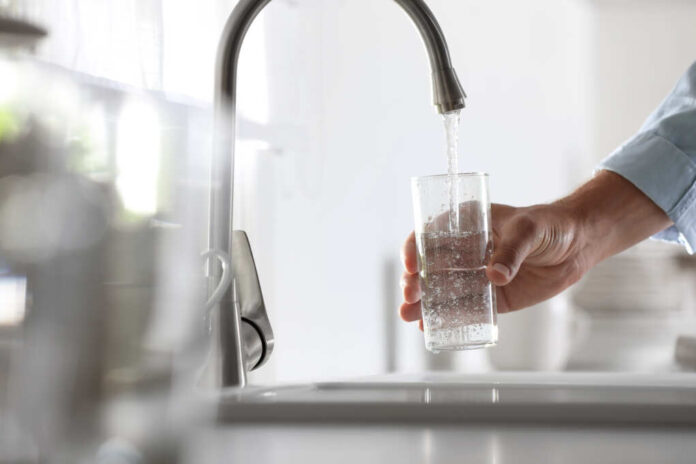 Man,Pouring,Water,Into,Glass,In,Kitchen,,Closeup