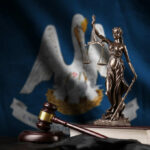 Bronze statue of Lady Justice with scales, a gavel, and books in front of the Louisiana state flag