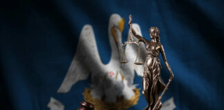 Bronze statue of Lady Justice with scales, a gavel, and books in front of the Louisiana state flag