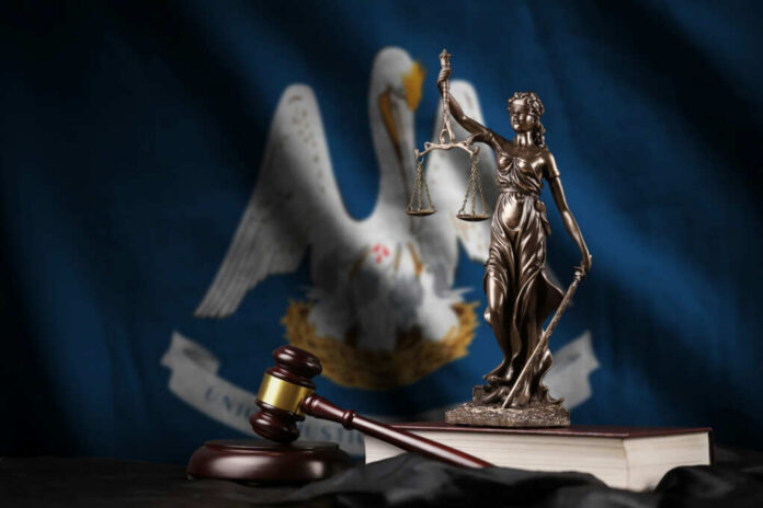 Bronze statue of Lady Justice with scales, a gavel, and books in front of the Louisiana state flag