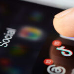 Close-up of a finger tapping a TikTok icon on a smartphone screen with social media labels