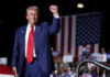 A man in a suit raises his fist at a political rally with an American flag in the background