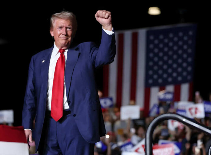 A man in a suit raises his fist at a political rally with an American flag in the background