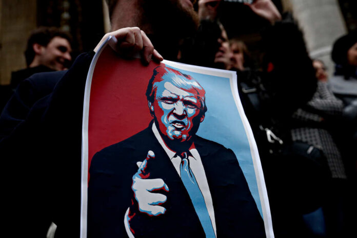 A person holding a protest sign featuring a stylized illustration of a man with a serious expression
