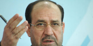 A political figure speaking at a press conference with a serious expression