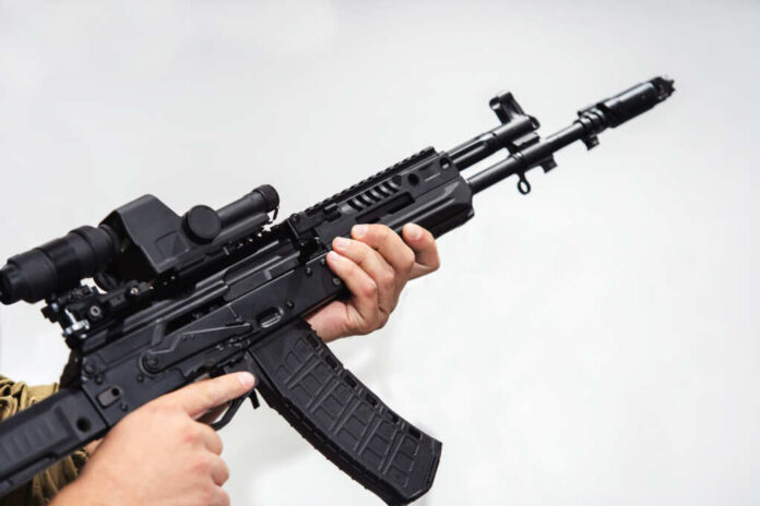 Person holding an AK-47 rifle with a scope