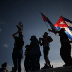 Cuba’s “Goodwill” Move – Is Trump Behind It? Silhouetted figures celebrating with a trophy and Cuban flags against a sunset sky