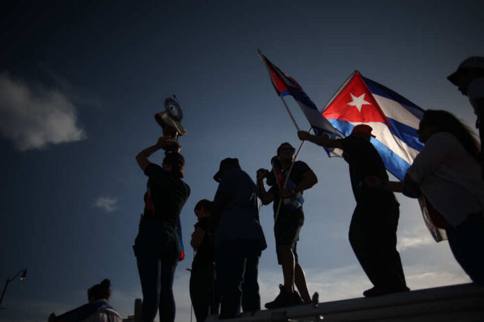 Silhouetted figures celebrating with a trophy and Cuban flags against a sunset sky