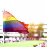 Rainbow flag waving in the foreground with a blurred crowd in the background