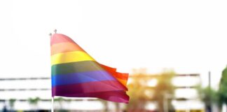 Rainbow flag waving in the foreground with a blurred crowd in the background