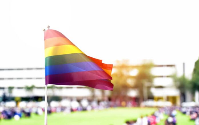 Rainbow flag waving in the foreground with a blurred crowd in the background