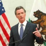 Governor’s Pet Project Sparks Outrage – Taxpayers FURIOUS! A government official delivering a speech with flags in the background