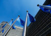 European Union flags flying in front of a modern building against a clear blue sky