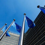 European Union flags flying in front of a modern building against a clear blue sky