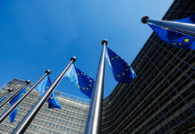 European Union flags flying in front of a modern building against a clear blue sky