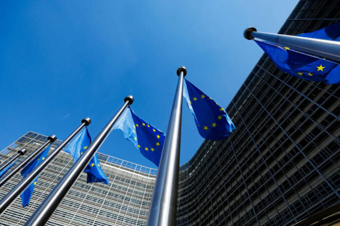 European Union flags flying in front of a modern building against a clear blue sky