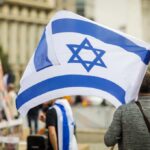 Israel Threatens Solo Strike—U.S. Changes Course Person holding an Israeli flag at a public demonstration