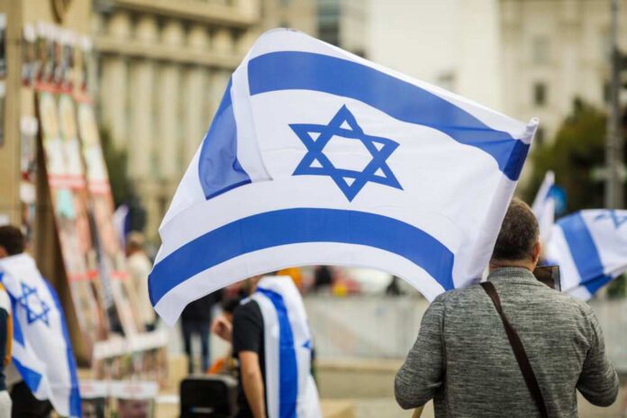 shutterstock_2385090811.jpg Person holding an Israeli flag at a public demonstration