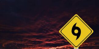 A yellow hurricane warning sign against a dramatic sunset sky