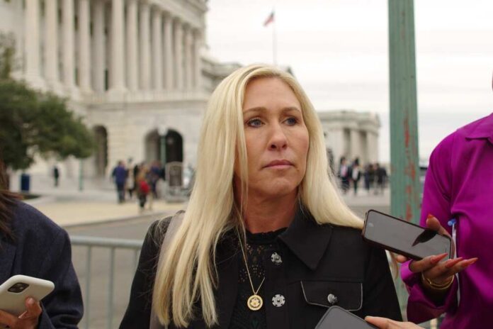 A woman with long blonde hair stands outdoors, surrounded by people holding smartphones.