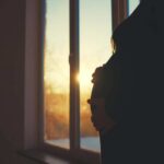 Silhouette of a pregnant woman standing by a window at sunset
