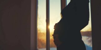 Silhouette of a pregnant woman standing by a window at sunset