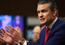 A man in a blue suit speaking passionately at a podium during a hearing
