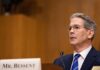 A man in formal attire speaking at a government hearing