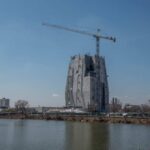 Obama’s Billion-Dollar Project Threatens Chicago Homes A large construction site with a crane and a partially completed building near a body of water
