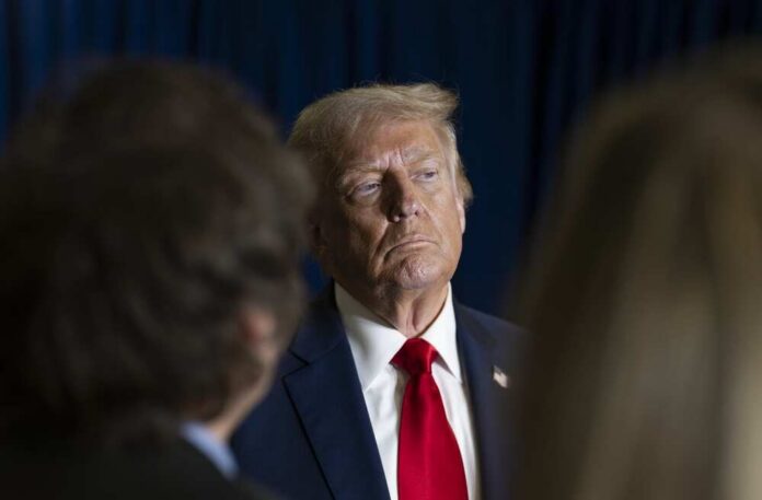 A serious-looking political figure in a suit and red tie during a media interaction