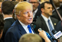 A man speaking to reporters at a press event surrounded by media personnel