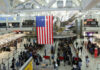 Busy airport terminal with travelers and a large American flag