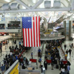 Massive TSA Walkout Leaves Airports Vulnerable Busy airport terminal with travelers and a large American flag