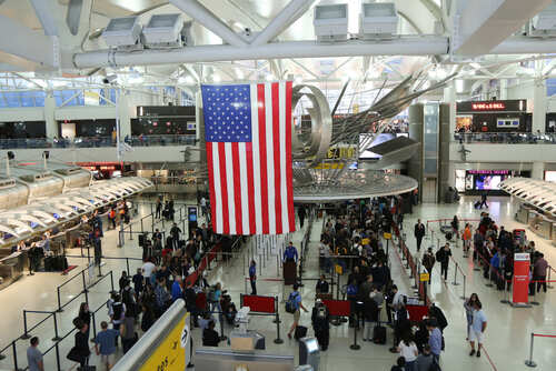 Busy airport terminal with travelers and a large American flag