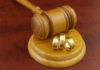 A wooden gavel next to three gold wedding rings on a wooden base