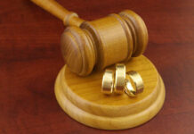 A wooden gavel next to three gold wedding rings on a wooden base