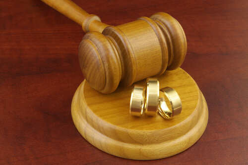 A wooden gavel next to three gold wedding rings on a wooden base