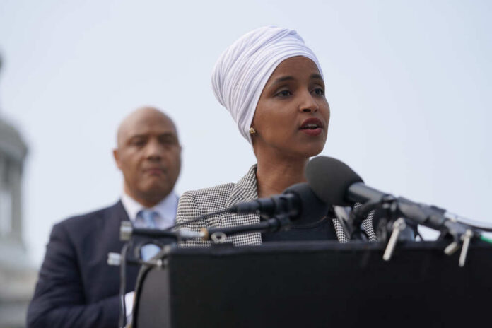 Ilhan Omar speaking at a press conference with André Carson in the background