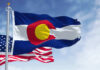 Flags of the United States and Colorado waving against a blue sky