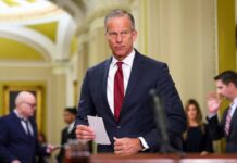 A male politician in a suit holding a notepad in a government building