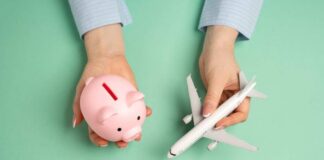 Hands holding a piggy bank and a toy airplane against a mint green background