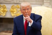 A man in a blue suit and red tie pointing while seated