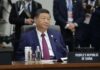 A seated leader at a conference table with a nameplate indicating the People's Republic of China