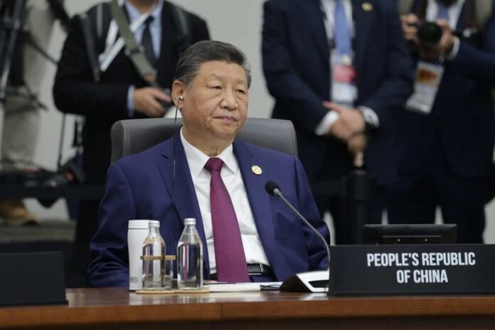 A seated leader at a conference table with a nameplate indicating the People's Republic of China
