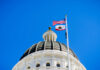 View of a state capitol dome with American and California flags against a blue sky