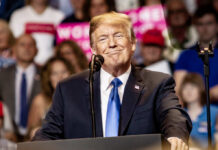 Mysterious C-SPAN Caller Sparks Trump Revolt Buzz A speaker smiling at a political rally with a microphone in front of him and an engaged audience behind.
