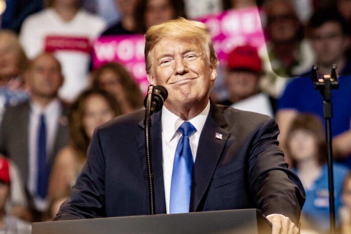 A speaker smiling at a political rally with a microphone in front of him and an engaged audience behind.
