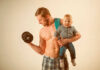 Internet EXPLODES Over Parenting Debate A muscular man lifting a dumbbell while holding a smiling baby