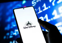 A smartphone displaying the Walt Disney logo with a blurred financial data background
