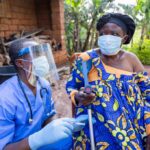 Ebola Horror: Camps in Congo LACK BASICS! Healthcare worker in PPE talks with elderly woman using a crutch outdoors